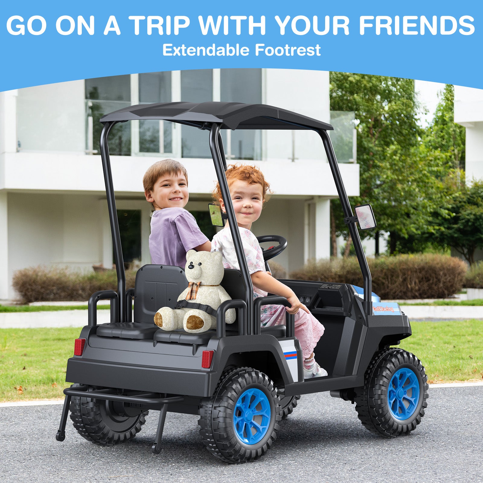 Two children in a toy utility vehicle with an extendable footrest, sitting on a driveway.