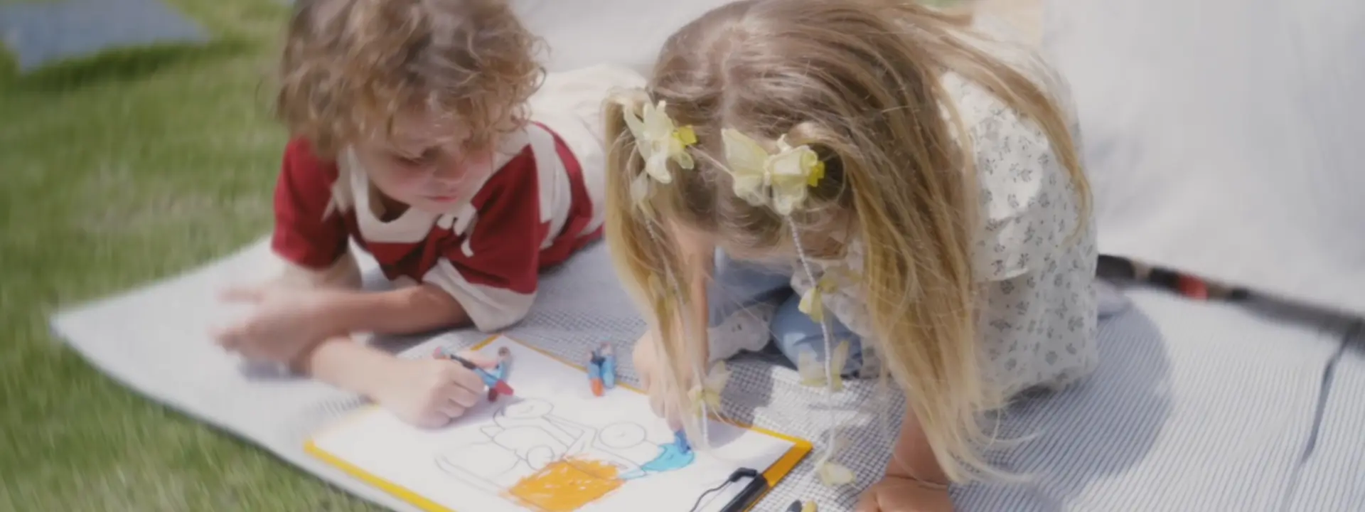 Two children drawing on a blanket outdoors