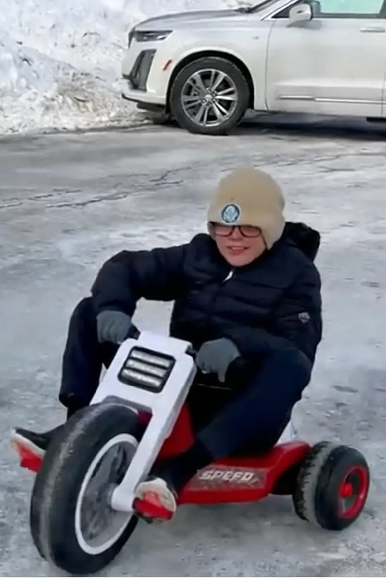 Child on a toy car in a snowy area with a vehicle in the background